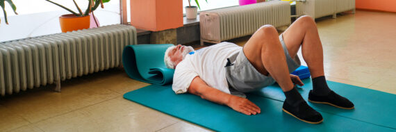 Older adult doing a supine pelvic tilt on a yoga mat, illustrating a physical therapy exercise for lumbar compression fractures.