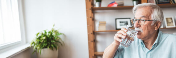 Senior man sipping water at home, emphasizing strategies for managing dysphagia to avoid risks and prevent complications.