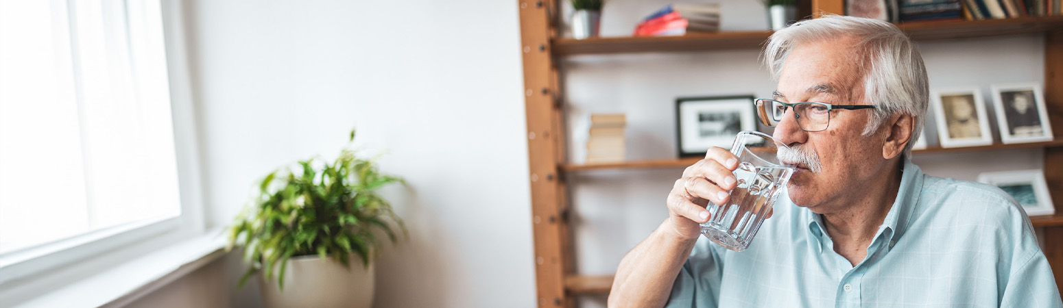 Senior man sipping water at home, emphasizing strategies for managing dysphagia to avoid risks and prevent complications.