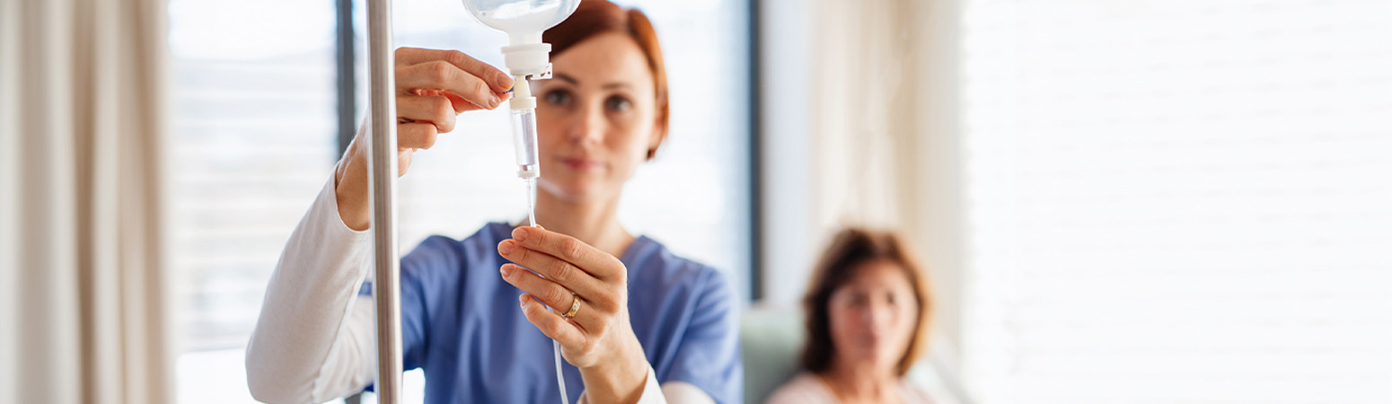 Nurse adjusting IV drip with a patient in the background, illustrating the choice between midline vs PICC lines in care.