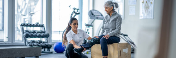 Physical therapist assists a senior patient in a gym setting, demonstrating exercises for ACL rehabilitation and knee recovery.