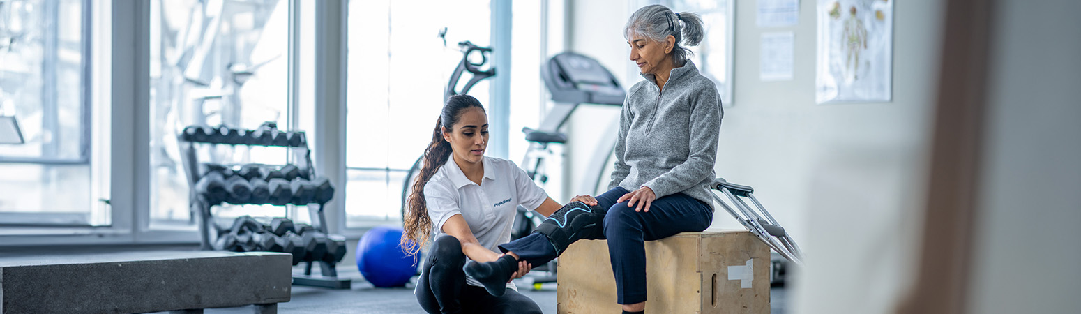 Physical therapist assists a senior patient in a gym setting, demonstrating exercises for ACL rehabilitation and knee recovery.