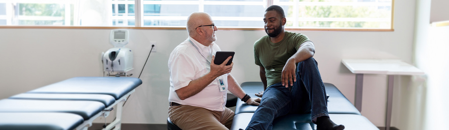 Rehabilitation professional using a tablet to demonstrate digital health skills to a patient during a consultation in a clinic.