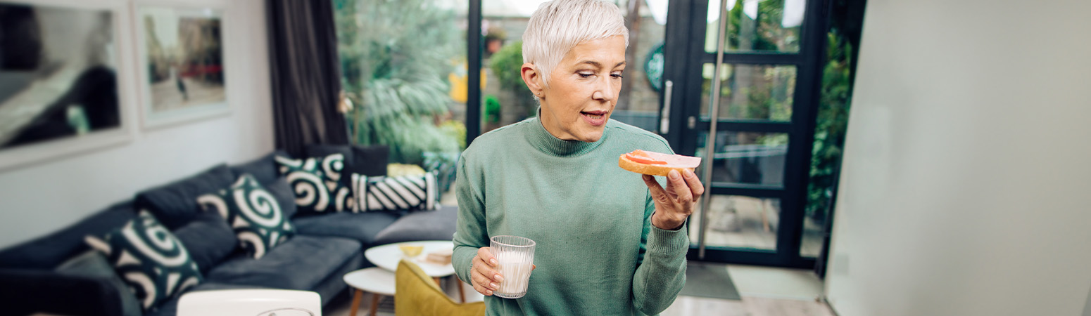 Older woman enjoying a snack while focusing on nutrition for bone health with a glass of milk and fruit.