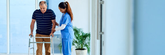 Healthcare provider assisting an elderly patient using a walker to improve mobility and reduce fall risks in a care facility.