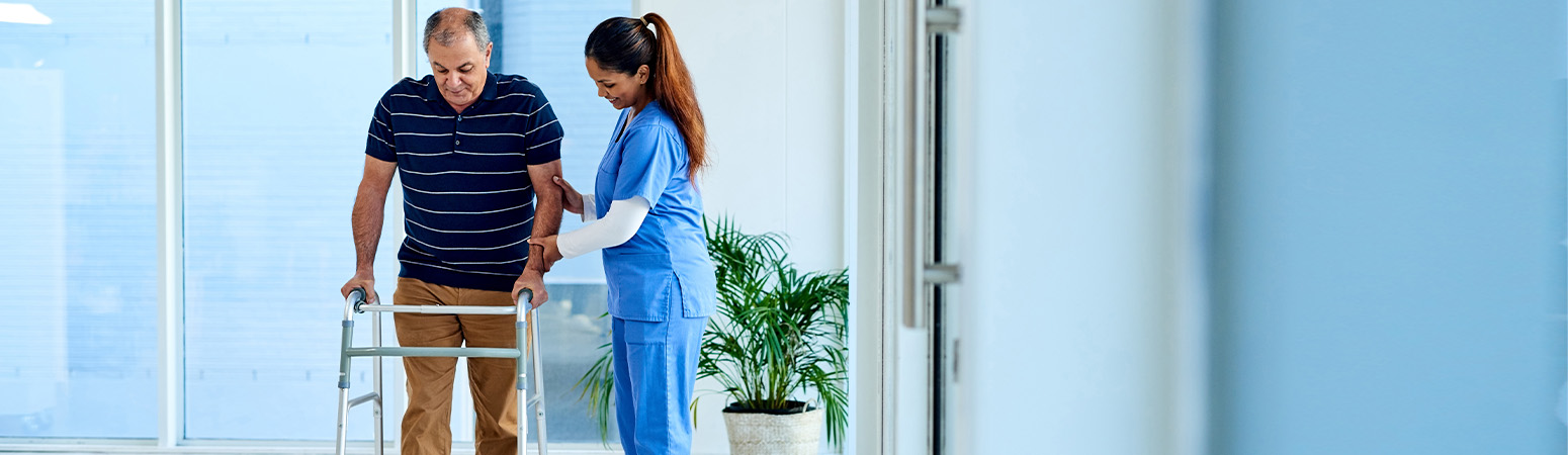 Healthcare provider assisting an elderly patient using a walker to improve mobility and reduce fall risks in a care facility.