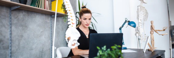 Physical therapist focused on billing at her desk, with spine model in view, emphasizing accurate physical therapy documentation.