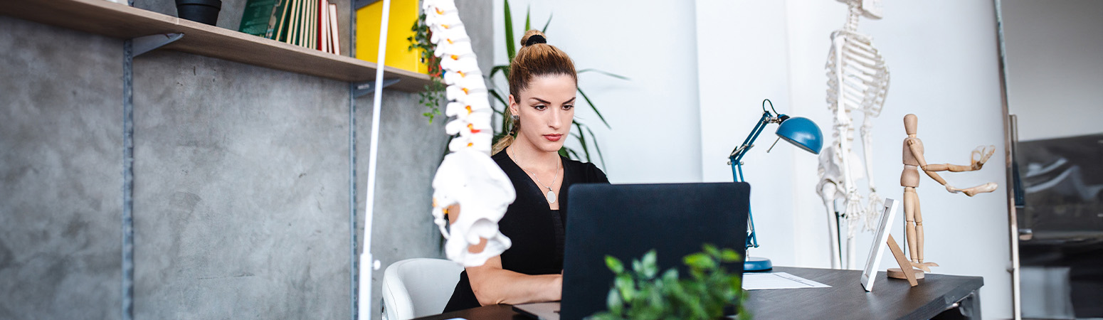 Physical therapist focused on billing at her desk, with spine model in view, emphasizing accurate physical therapy documentation.