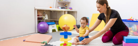 A therapist assists a child with cerebral palsy during physical therapy, encouraging motor skill development with colorful toys.