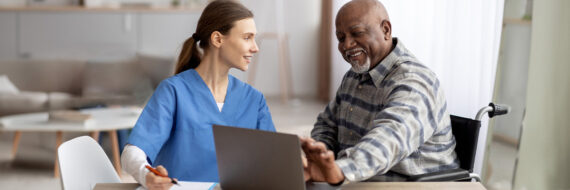 Healthcare practitioner in blue scrubs discussing telehealth options with a smiling senior patient in a wheelchair.