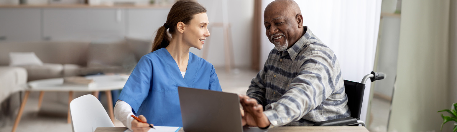 Healthcare practitioner in blue scrubs discussing telehealth options with a smiling senior patient in a wheelchair.