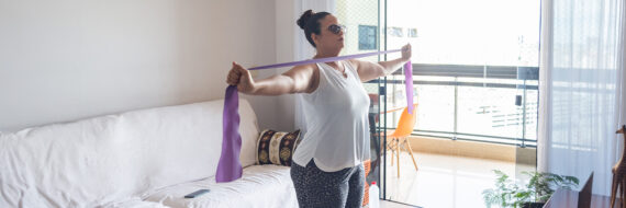 Woman performing exercises for shoulder mobility and pain relief using a resistance band at home.