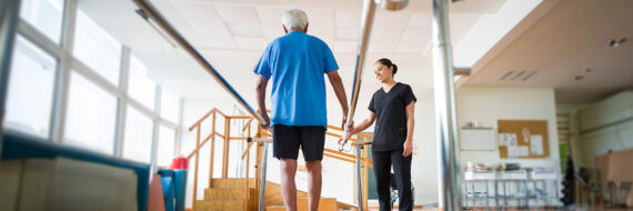 Physical therapist assisting an older adult with balance exercises using parallel bars, emphasizing rehabilitation and mobility.