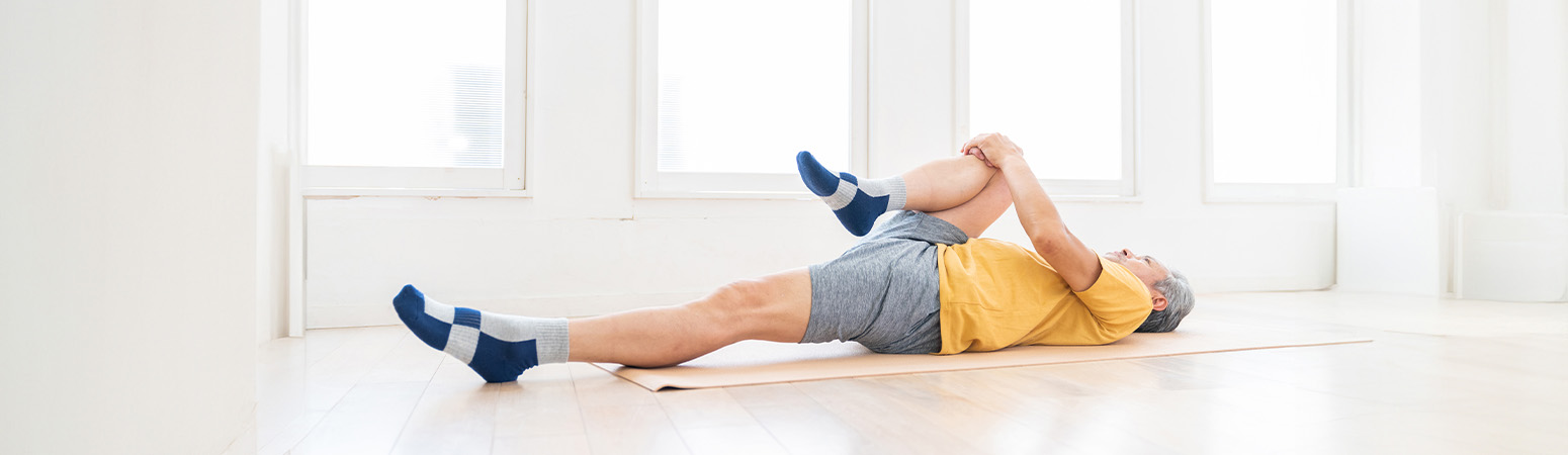 A person performing a supine single knee-to-chest stretch, an exercise for relieving low back pain and improving mobility.