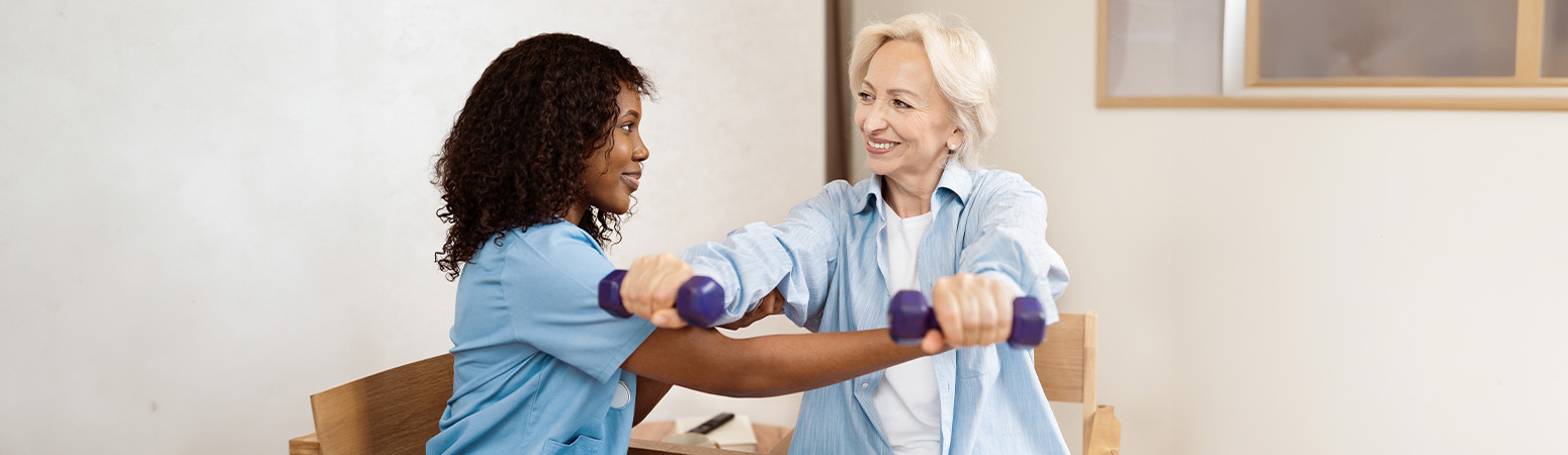 Occupational therapist assisting an older adult with strength exercises using hand weights during therapy.