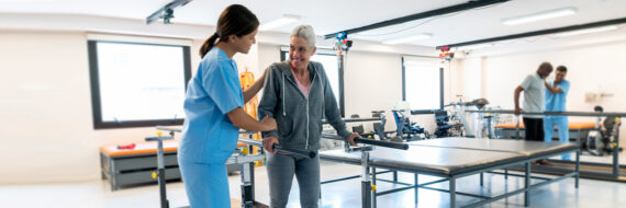 A therapist guiding a patient in a rehab facility with parallel bars for hip mobility and recovery exercises.