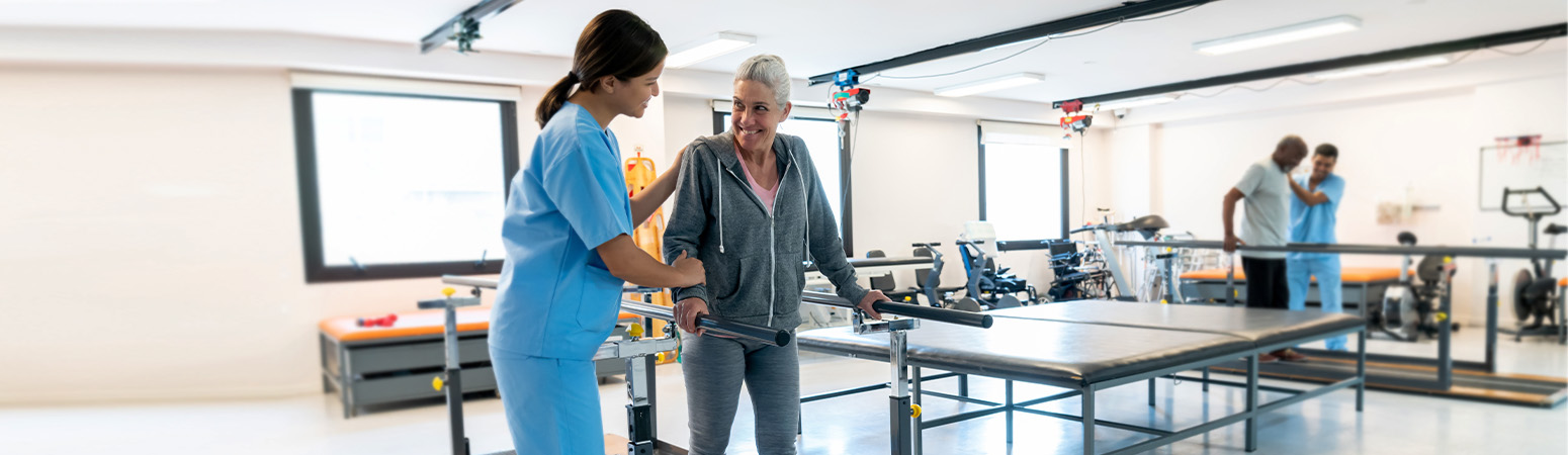 A therapist guiding a patient in a rehab facility with parallel bars for hip mobility and recovery exercises.