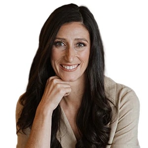 A smiling person with long dark hair, hand on chin, against a plain background.