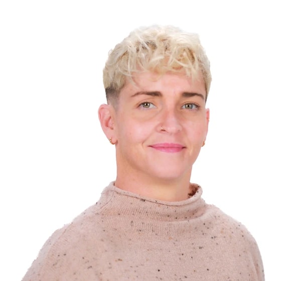 A person with curly blonde hair and a pink speckled turtleneck smiles softly, reflecting the warmth of Medbridge's patient care software.