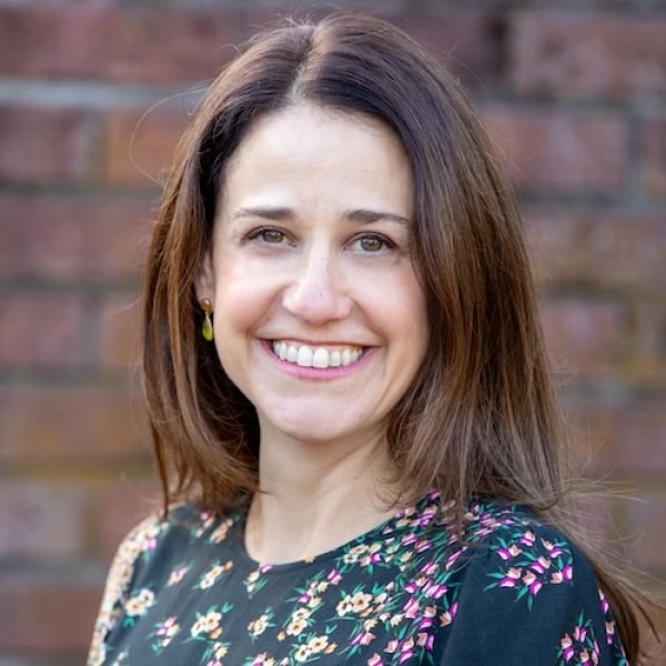 A smiling woman in a floral top stands against a brick wall, representing the future of digital healthcare for Medbridge.