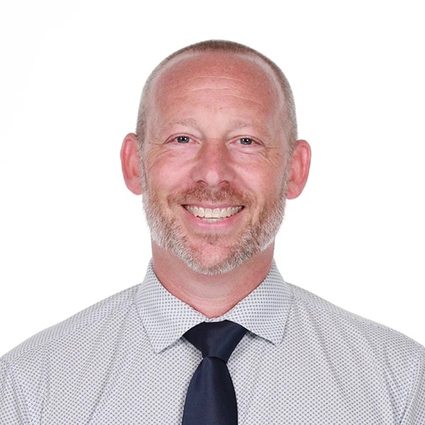 A bearded man in a dotted shirt and tie stands confidently, suggesting expertise in healthcare or medbridge software.