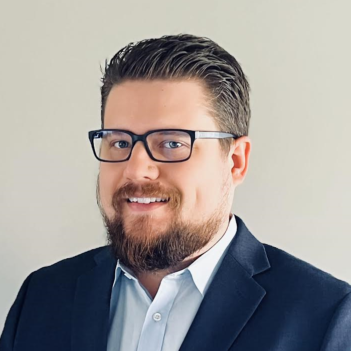 A bearded man in glasses and a suit smiles confidently, embodying digital healthcare expertise, representing medbridge.